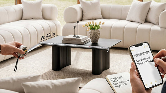 Close-up of hands logging coffee table measurements into a notebook and phone, with a modern textured plinth base table styled with yellow tulips.