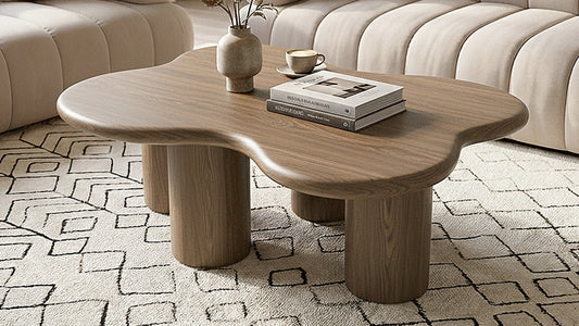 A walnut-finished coffee table with a kidney-bean-shaped design, styled with a candle and coffee table books.