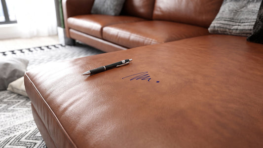 Blue ink stain and a pen resting on the cushion of a tan leather sectional sofa.   