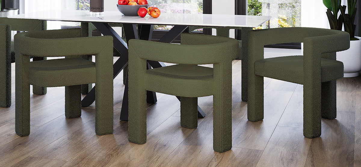 Modern dining nook with a white, glossy rectangular table and four olive-green upholstered chairs. A bowl of red apples sits atop the table, with garden views outside.