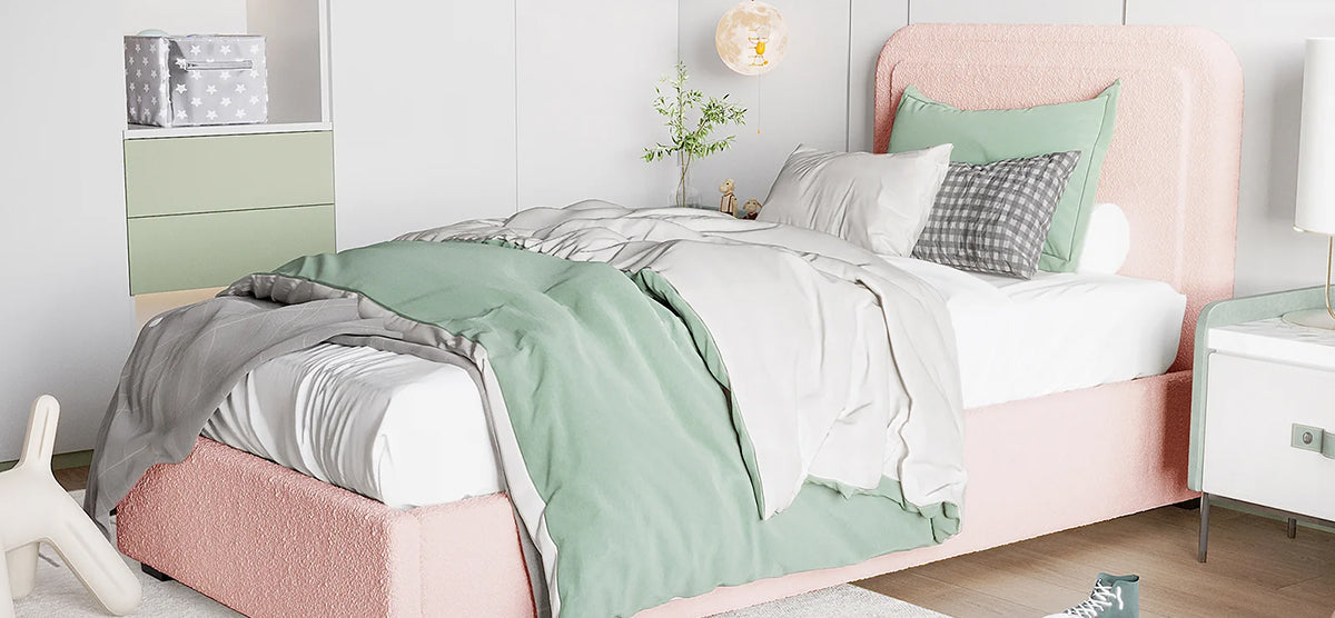 A modern bedroom corner with a pink upholstered bed, white nightstand, green wall cabinet, and a light rug on wood floor, hinting at a youthful, pastel theme.