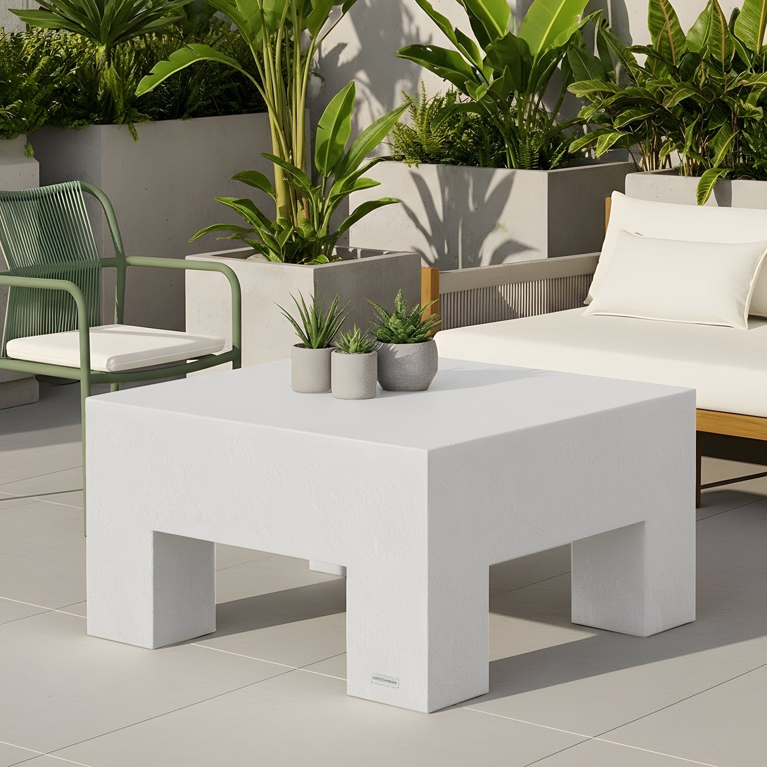 White square coffee table with chunky block legs and a textured stone-look finish, styled with small potted plants on a patio.