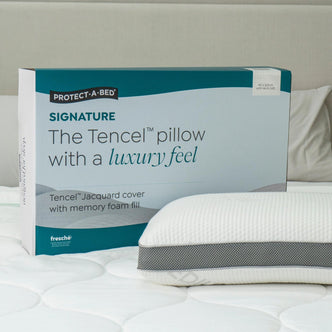 Protect-A-Bed Signature Tencel jacquard memory foam pillow, Medium, in its packaging box next to the pillow on a bed