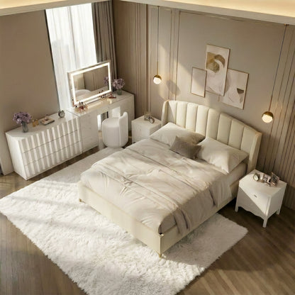 Contemporary bedroom with a vertical channeled cream velvet bed headboard, a fluted white dresser, and a matching lit vanity mirror. The room is decorated with gold pendant lights, a patterned neutral rug, and warm wood flooring under soft ambient lighting.