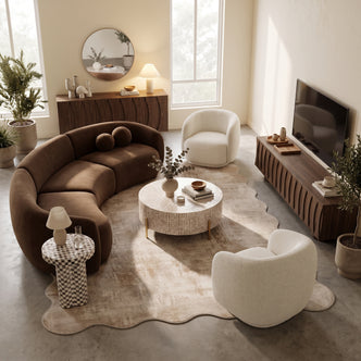 Curved brown velvet sectional sofa paired with two cream bouclé armchairs, a round coffee table, and a wooden TV unit in a neutral living room space.