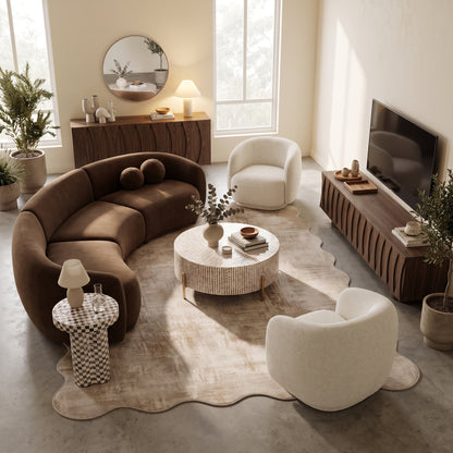 Curved brown velvet sectional sofa paired with two cream bouclé armchairs, a round coffee table, and a wooden TV unit in a neutral living room space.