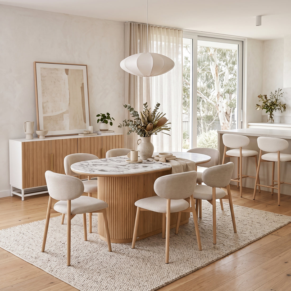 Oval marble-top dining table with a fluted wooden base and cream bouclé chairs in a modern open-plan interior.
