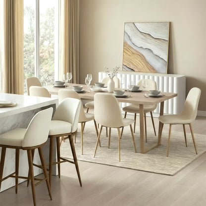 Modern organic dining room featuring a light oak wood rectangular table paired with cream upholstered dining chairs on gold legs. In the background, a white fluted sideboard stands below a large abstract textured painting in gold and grey, set on a neutral textured area rug.