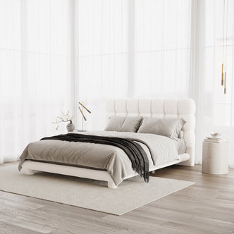 Aina Queen Boucle Bed Frame in Cream White features a plush tufted headboard, dressed in neutral linens with a charcoal throw. Side tables with decor flank the bed, creating a serene, airy bedroom setting.