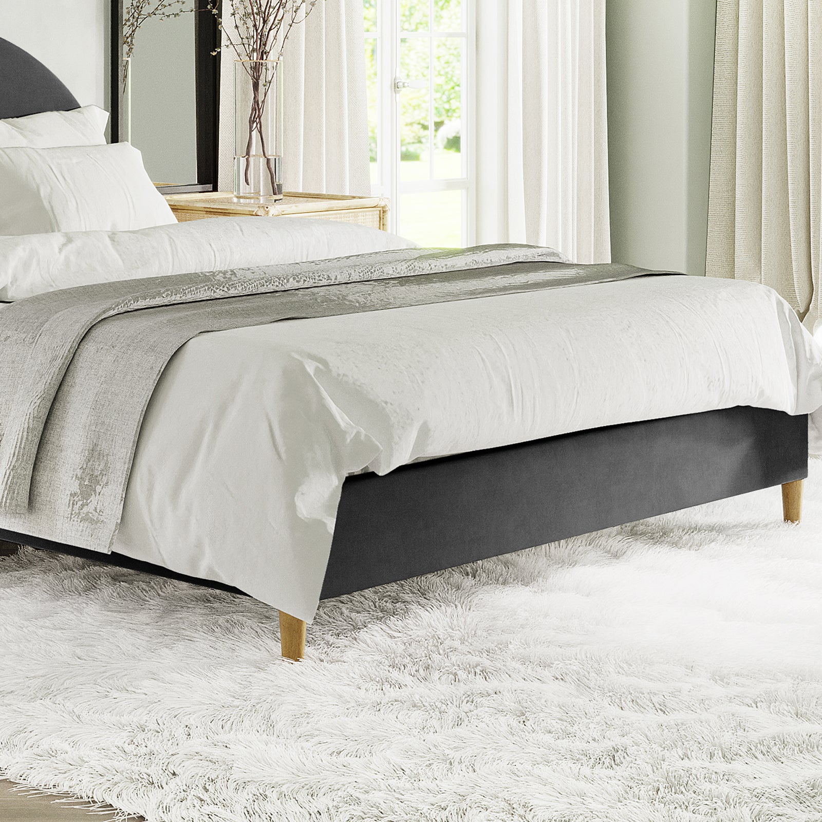 Celina Boucle Upholstered Fabric Bed Base - Black Queen in a serene bedroom, featuring a low-profile design with natural wood legs, dressed in white linens, complemented by a fluffy white shag rug.