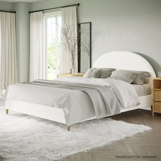 Celina Queen Boucle Fabric Bed Base in Cream White, featuring textured upholstery, low-profile design, plush linens, and sturdy timber legs, nestled on a shaggy rug in a bright, minimalist bedroom setting.