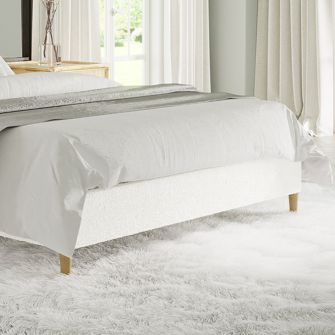 Celina Queen Boucle Fabric Bed Base in Cream White features boucle upholstery, wooden legs, and foam padding, set on a fluffy white rug with a decorative runner at the bed's foot.