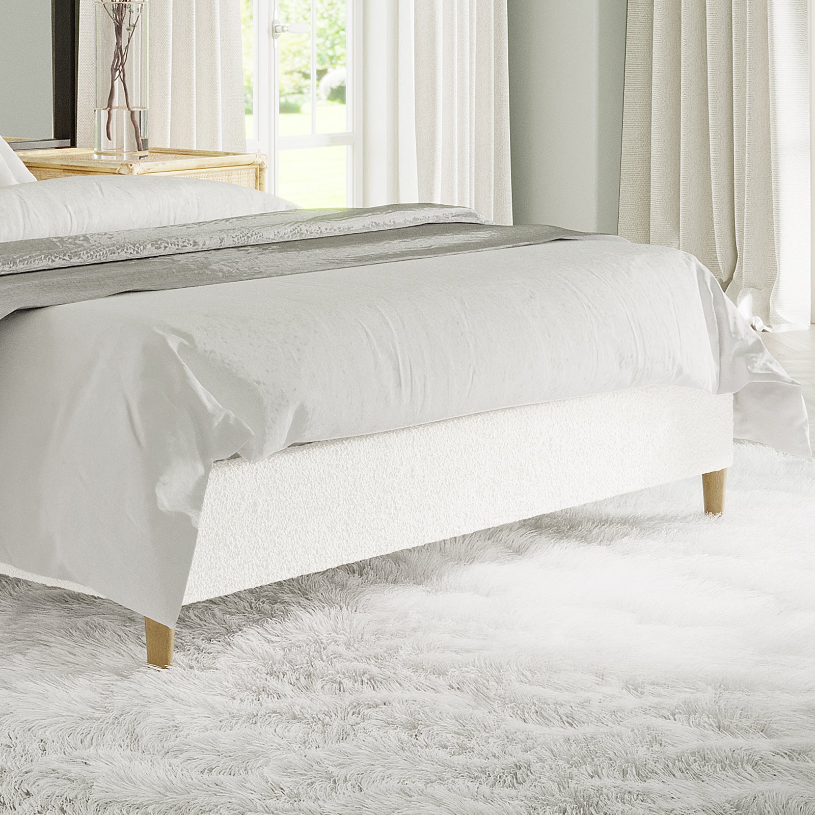Celina Queen Boucle Fabric Bed Base in Cream White features boucle upholstery, wooden legs, and foam padding, set on a fluffy white rug with a decorative runner at the bed's foot.