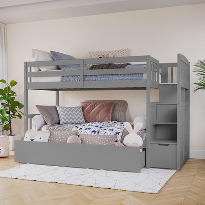 Flavia Solid Pine Wood Staircase Storage Bunk Bed in Grey features a top bunk with guardrails, a cozy trundle with cushions and toys, and a storage staircase, all on a light wood floor.