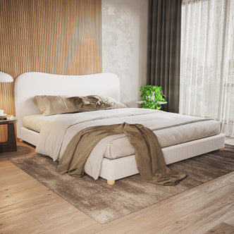 Ginnie Bouclé Curved King Bed Frame - Cream White in a minimalist bedroom with ribbed wood accent wall, neutral bedding, wooden bedside table, and soft natural light from floor-to-ceiling windows.