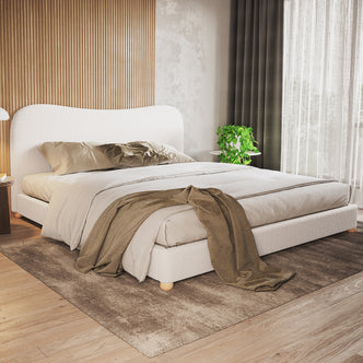 Ginnie Curved Bouclé Bed Frame - Cream White, features a low-profile design with a curved headboard, upholstered in soft bouclé fabric. Styled with neutral linens and a taupe-brown throw in a minimalist bedroom.