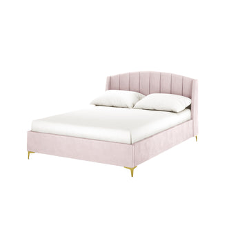 Lyra Velvet Bed Frame with Winged Headboard - Soft Pink Double, showcasing a blush-pink vertically tufted headboard, white linens, and slender brushed brass legs, ideal for minimalist, feminine bedroom decor.