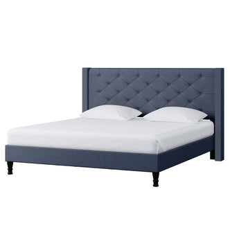Maggie King Winged Fabric Bed Frame – Dark Blue features a deep blue, button-tufted headboard, platform base, and black legs, accompanied by a white mattress and pillows, embodying sophistication and grandeur.