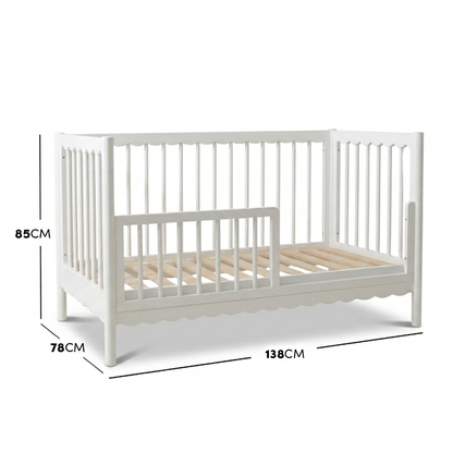 White timber toddler bed with scalloped base molding and dimensions diagram.