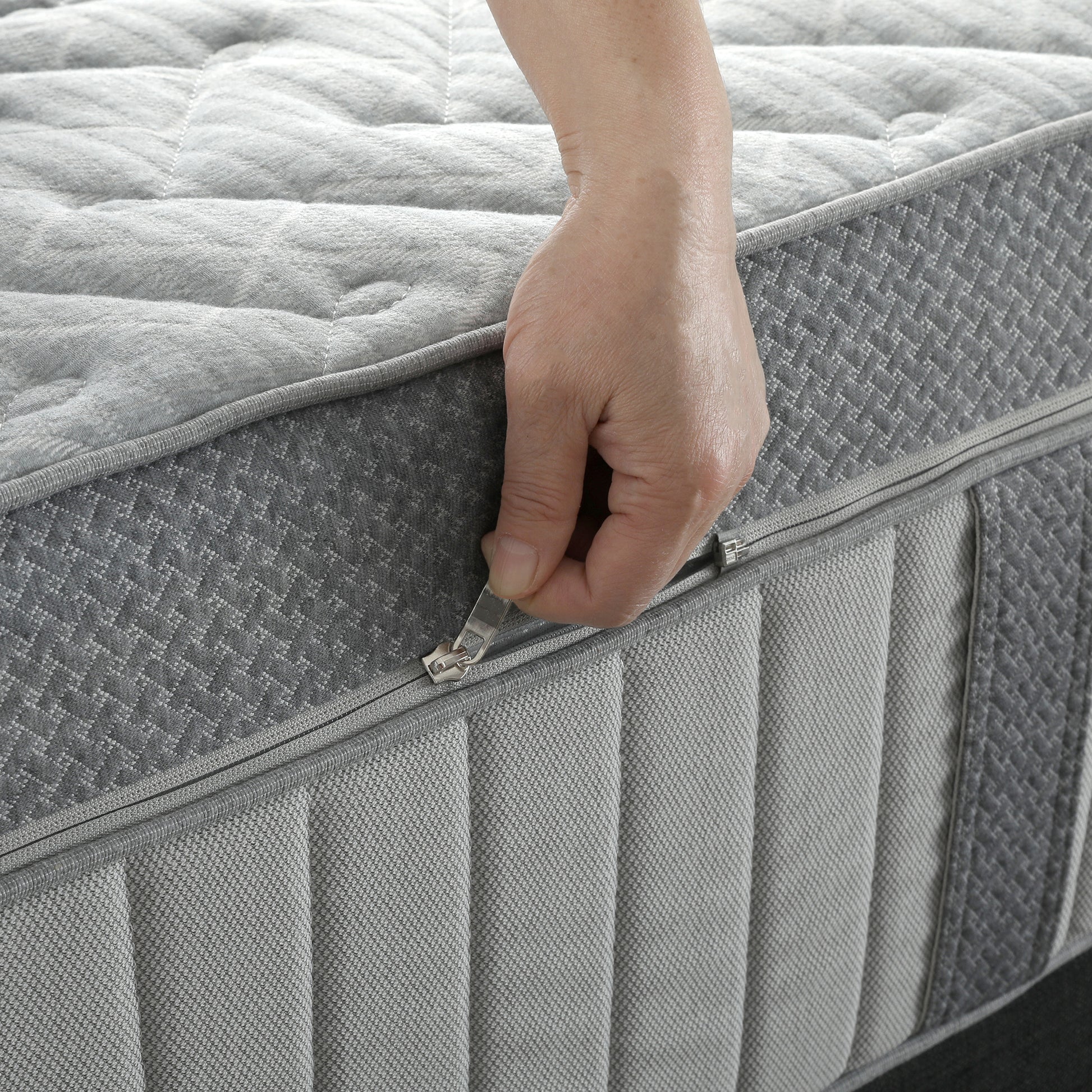 Detailed view of a hand unzipping the textured fabric top layer of a pocket spring mattress.