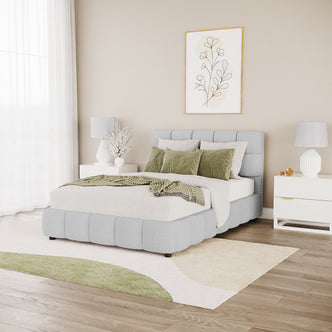 Nikias Double Bouclé Fabric Bed Frame in Light Grey with a tufted headboard and footboard, styled with light linens and green accents, flanked by white nightstands and lamps in a modern bedroom setting.