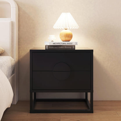 Abigail 55cm 2-Drawer Bedside Table - Black; features circular drawer details, topped with books and a star-like ornament, alongside a pleated lamp, complementing a modern bedroom setup.