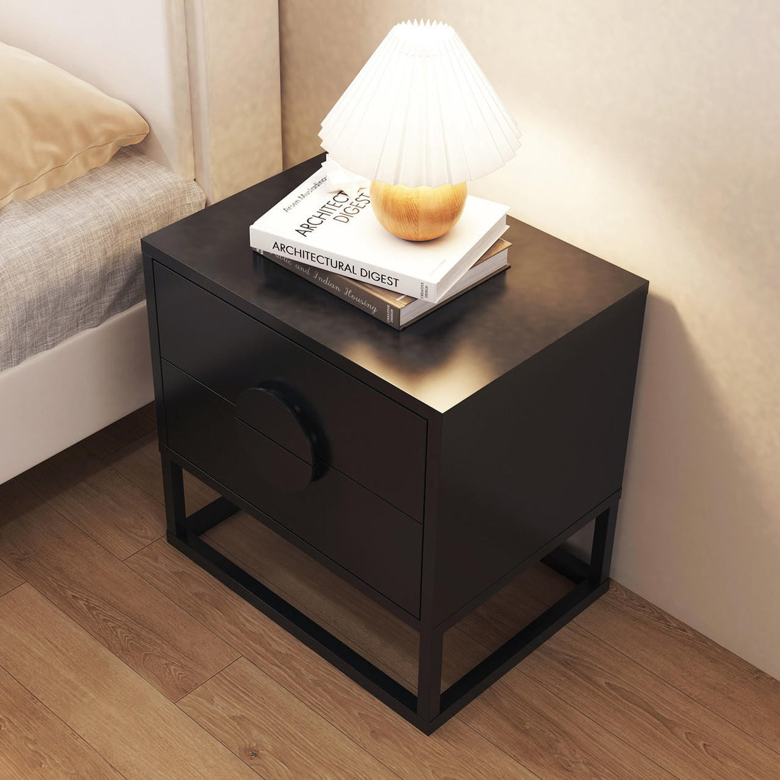 Abigail 55cm 2-Drawer Bedside Table w/ Handle - Black beside a bed, featuring two books and a table lamp on top, showcasing its modern design with metal frame and arc handles.