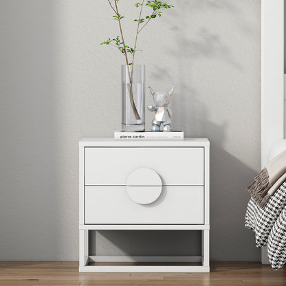 The Abigail 55cm 2-Drawer Bedside Table in white features sleek arc handles, topped with a glass vase, pierre cardin book, and silver bear figurine, complementing a minimalist bedroom setting.