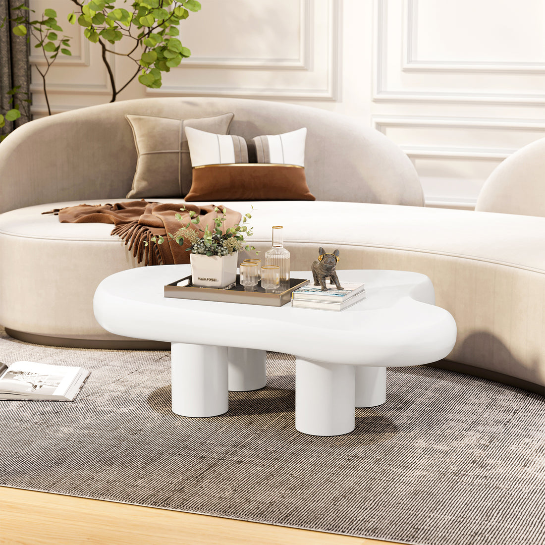 Blissey 90cm Organic Curved Cloud Coffee Table in White features a sculptural design with a sleek, cloud-shaped top on short cylindrical legs, accompanied by a metal tray, plant, and decor items.
