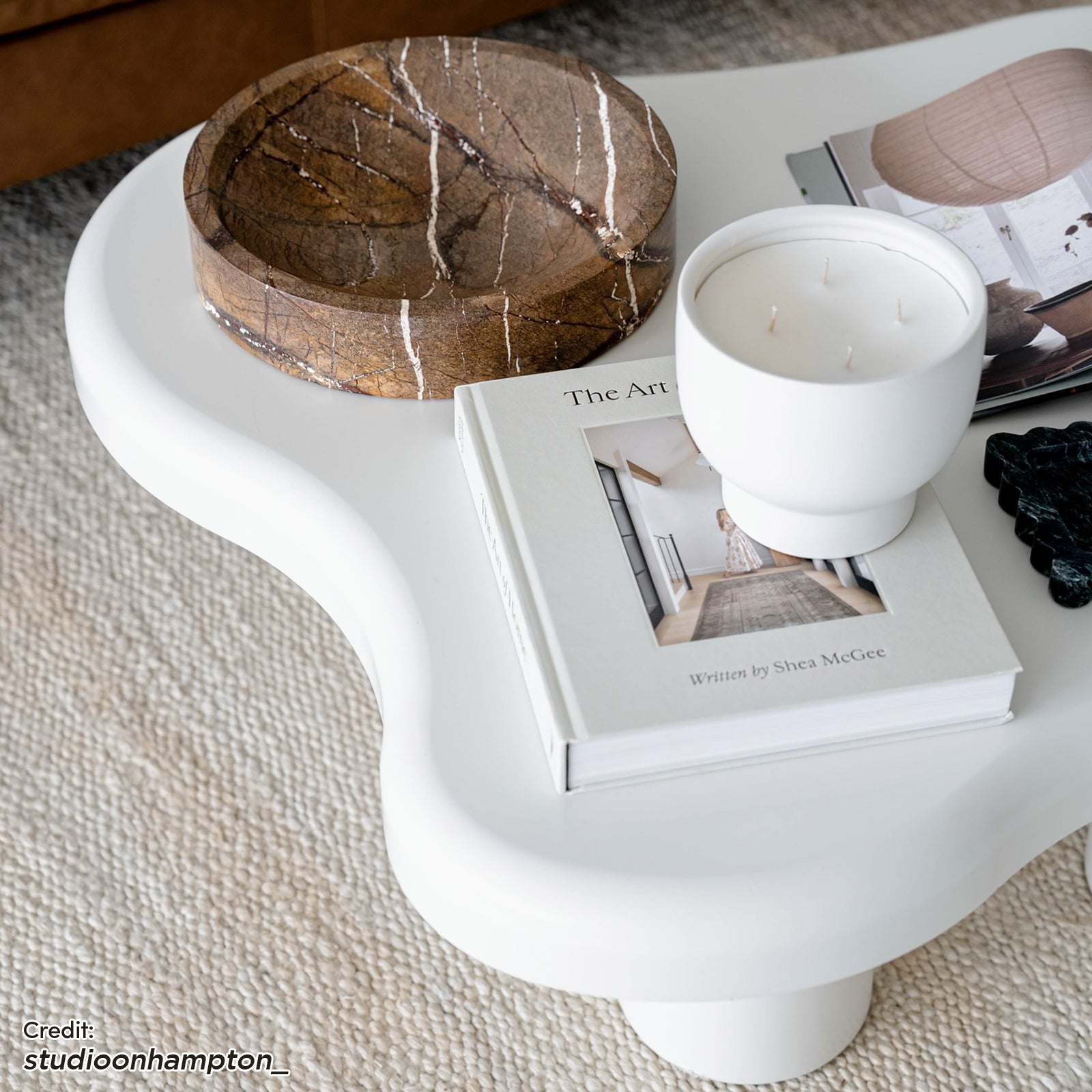 Blissey 90cm Cloud Coffee Table in White, featuring softly scalloped edges, on a woven rug; topped with a wooden platter, a book, a ceramic candle, and an open magazine.