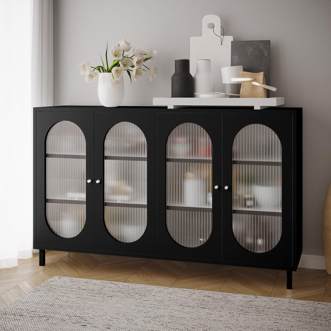 Cambria 150cm Fluted Glass Buffet Cabinet - Black with four ribbed glass doors, topped with a white vase of tulip-like flowers, decorative bottles, and a serving tray on a herringbone floor.