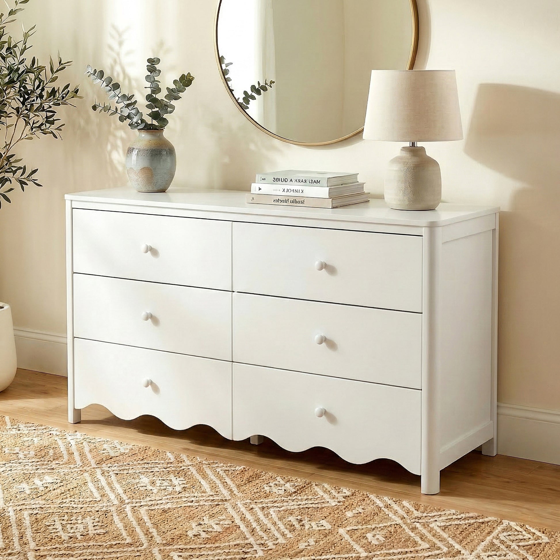 White dresser styled in a cozy room with vase, books, lamp, and round mirror