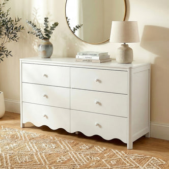 White dresser styled in a cozy room with vase, books, lamp, and round mirror