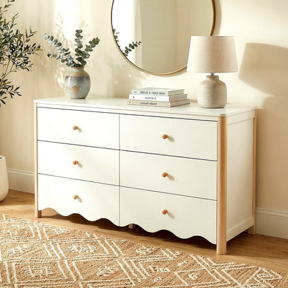 White six-drawer dresser with wood handles in a styled room with rug, lamp, and mirror