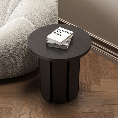 Hugo 45cm Round Side Table with Curve Detail in Black on herringbone floor, beside white boucle armchair, topped with two books, featuring Another Art Book prominently visible.