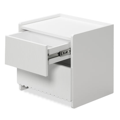 Nasrin 2 Drawer Bedside Table in White features a minimalist design with vertically fluted drawer fronts, short block-style legs, and a partially open top drawer revealing metal slides.