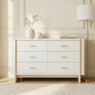Six-drawer dresser styled in a bright room with cream paneled walls, decorative vase, and floor lamp