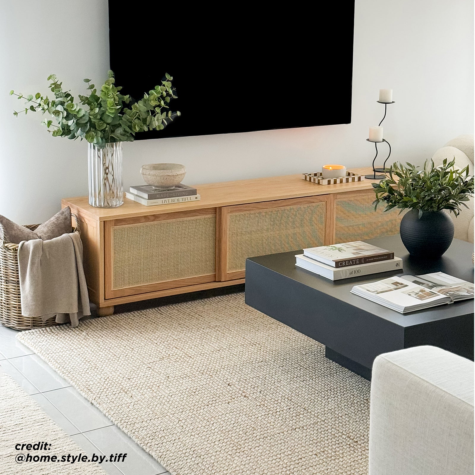 The Thea 200cm Solid Oak Rattan Entertainment Unit - Natural features elegant rattan sliding doors and sturdy timber legs, perfectly blending with modern interior design elements like houseplants and a couch.