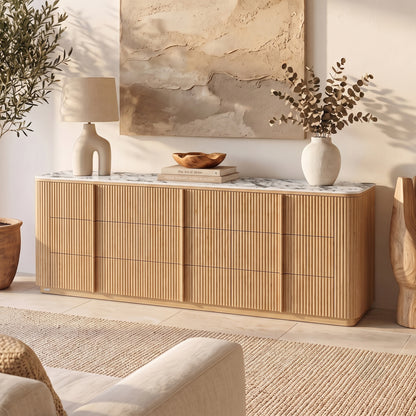 Natural fluted wood sideboard with white marble top and rounded corners in sunlit room