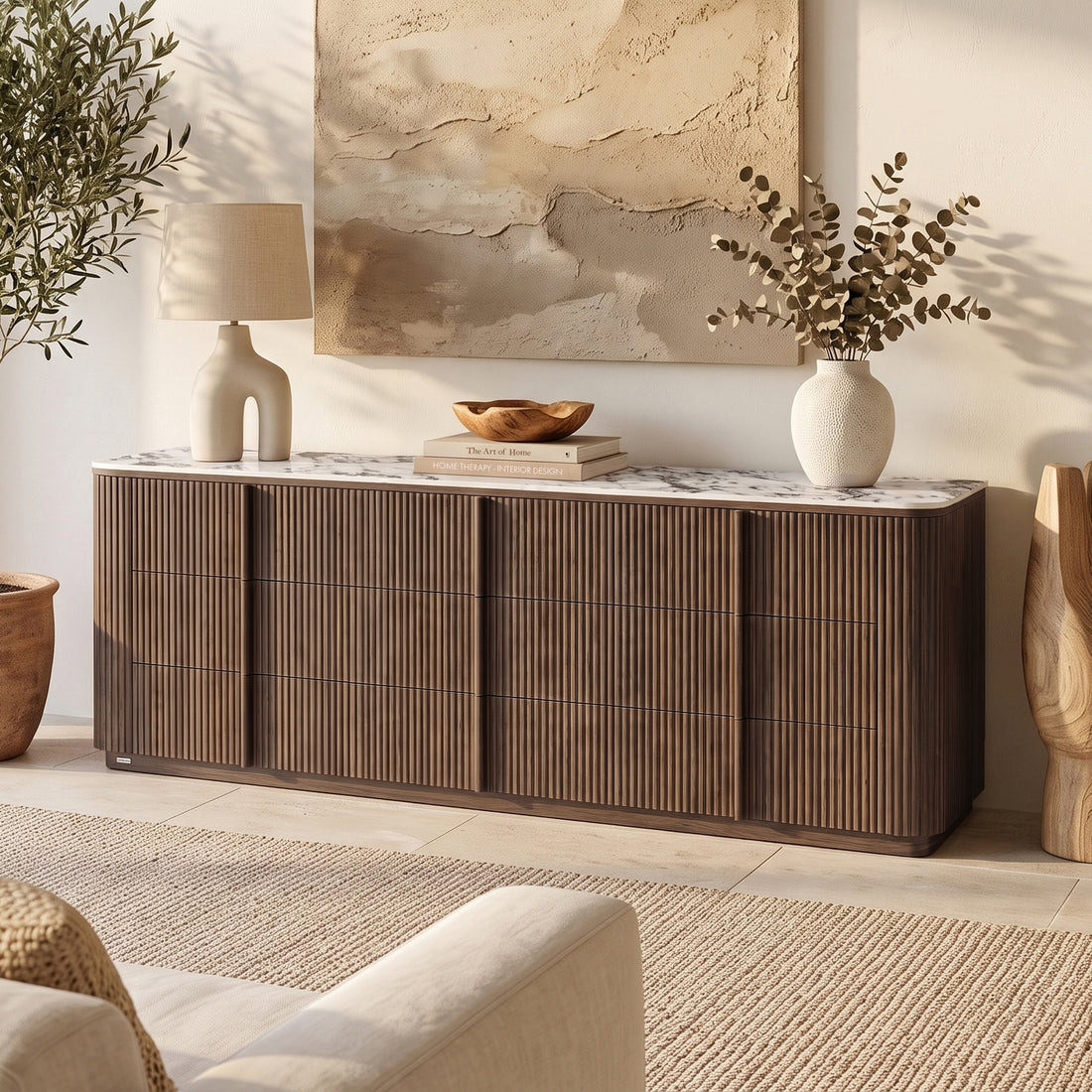 Walnut sideboard with fluted front, marble top, curved edges, four drawers. Styled with lamp, books, bowl, vase. Wall art
