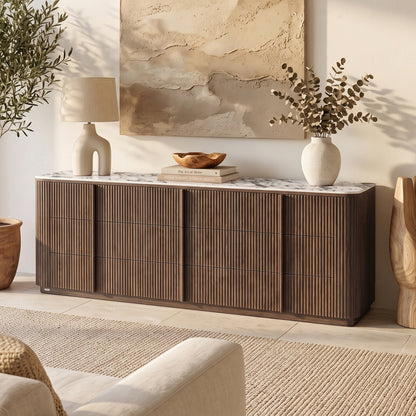 Walnut sideboard with fluted front, marble top, curved edges, four drawers. Styled with lamp, books, bowl, vase. Wall art