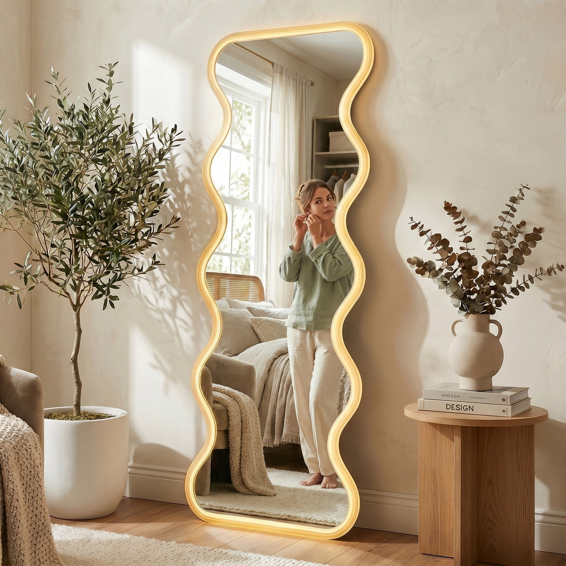 Davor 160cm Organic Waves Full Length LED Mirror in White, featuring a back-lit wavy frame. Reflects a woman adjusting earrings, enhancing the room's elegance with adjustable LED lighting for varied ambiance.