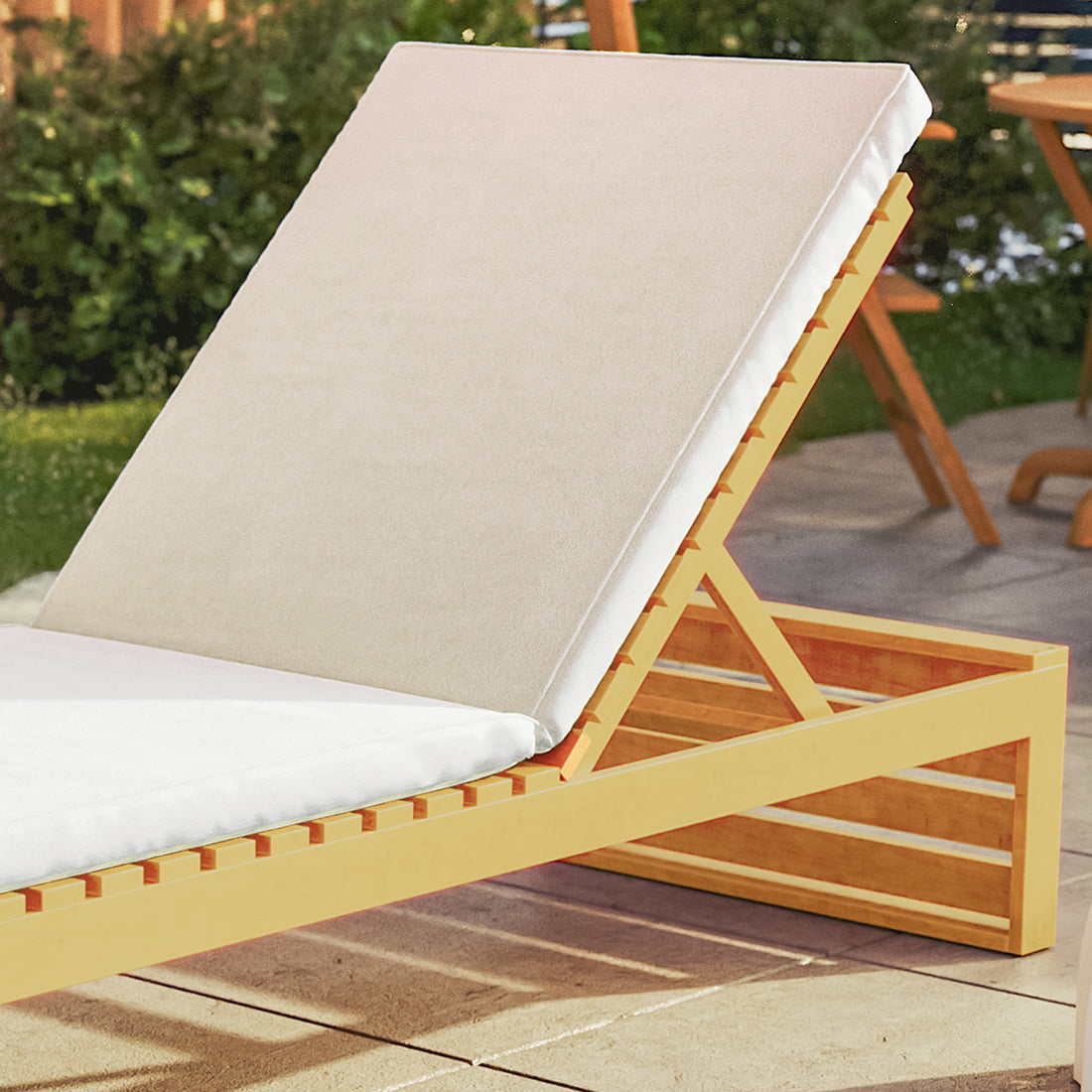 Alabat Hardwood Outdoor Sun Lounger Set of 2 in Cream, featuring a slatted wooden frame with a hinged backrest and light cushions on a patio with shrubbery and a small table.