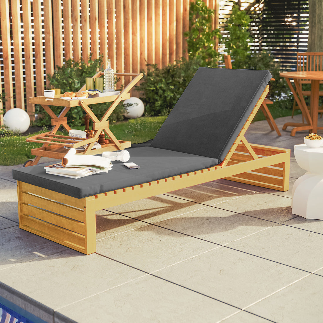 Alabat Acacia Wood Outdoor Sun Lounger with Cushion in Grey, featuring a propped backrest, dark gray cushion, and accompanying smartphone, headphones, and open book, set by a poolside with a serving cart.