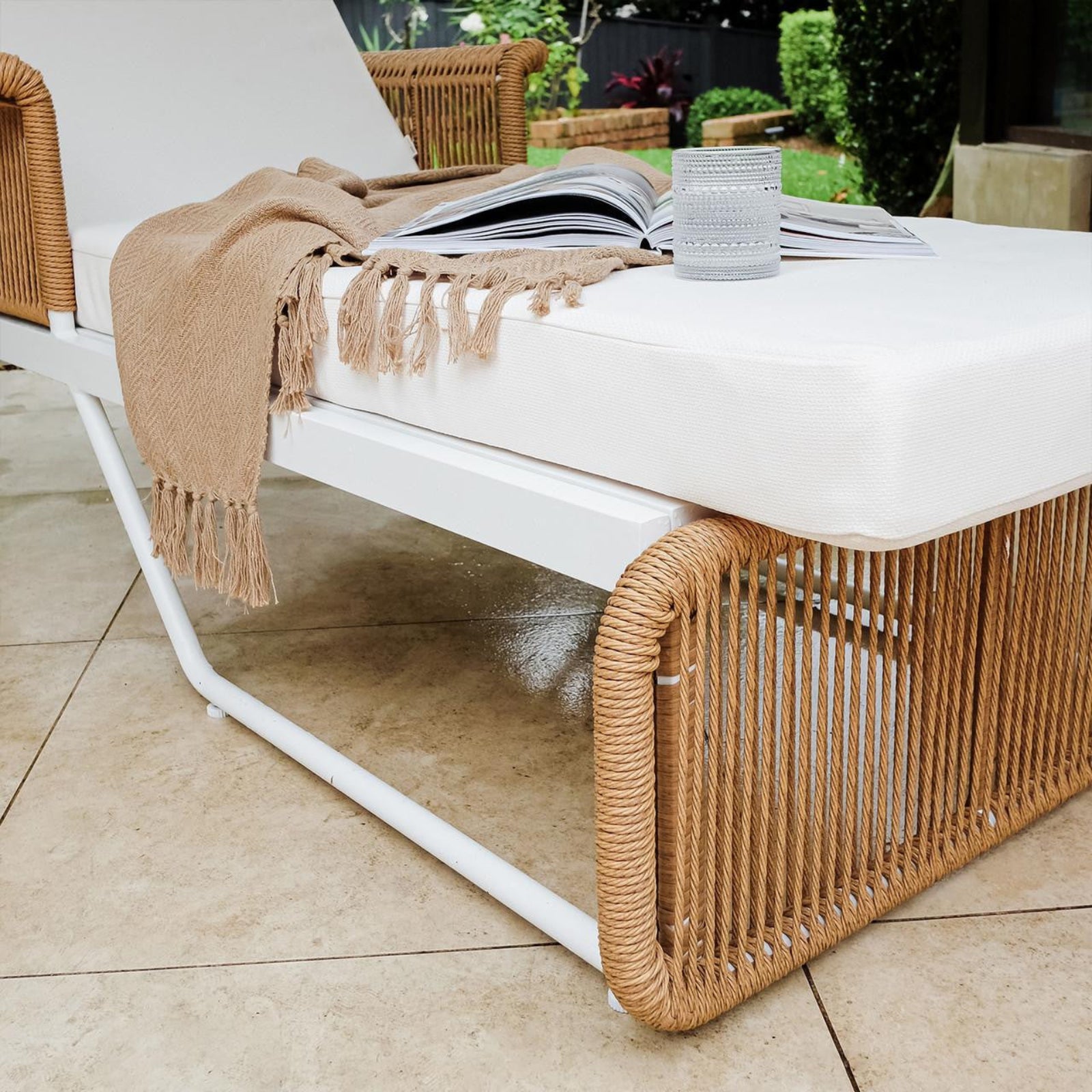 Boonoo Premium Aluminium Outdoor Rattan Sun Lounger featuring a sleek, adjustable design with rattan weave, visible soft cushions, and sturdy armrests, set on a patio floor with other outdoor furniture elements.