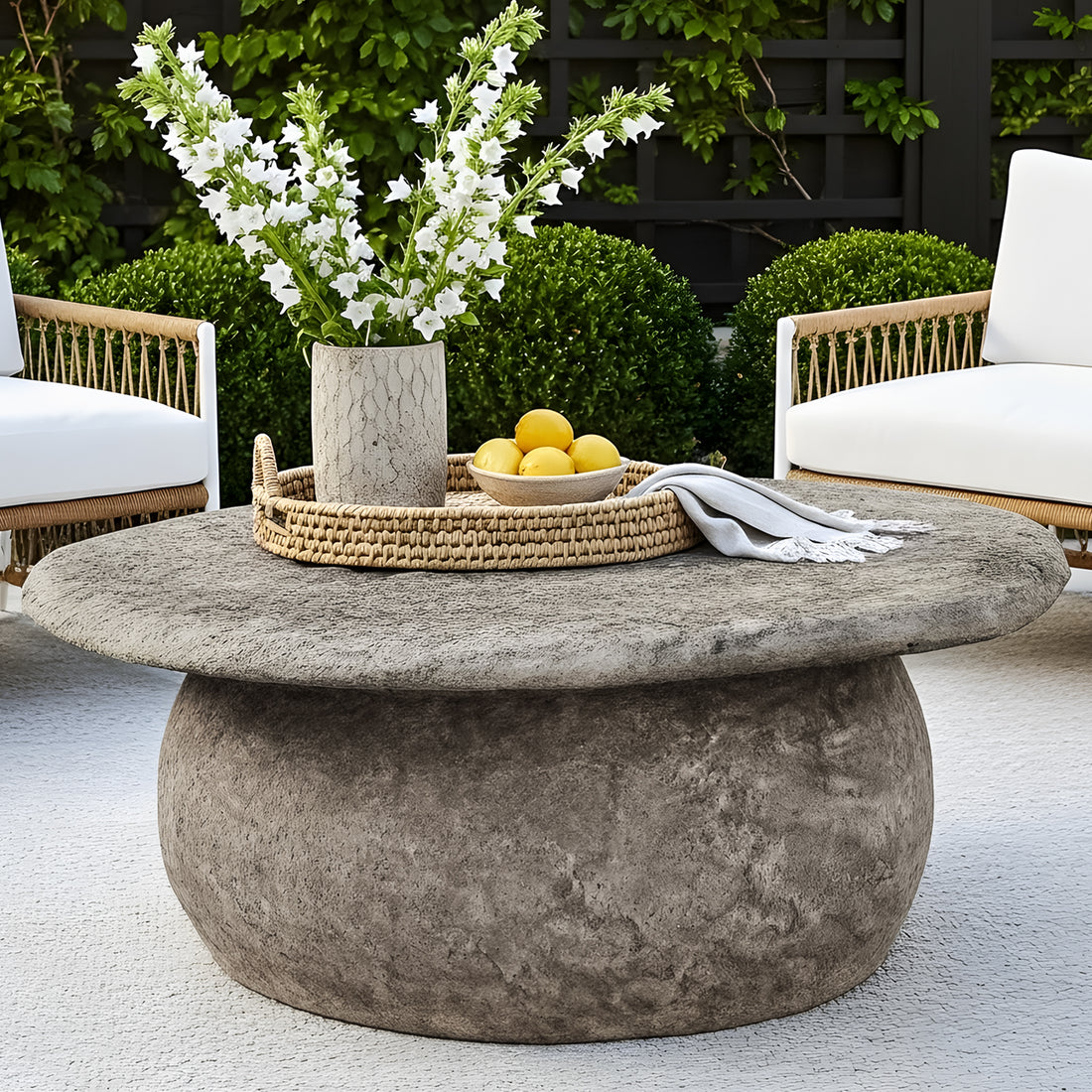Round outdoor coffee table with a textured grey stone finish and a thick, boulder-style pedestal base.