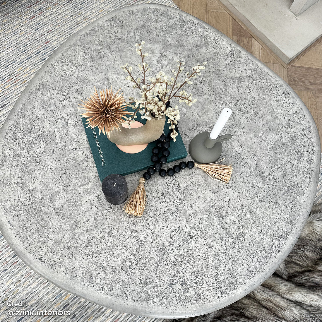 Cam Indoor & Outdoor Round Concrete Coffee Table - Stone, featuring a round, textured concrete surface, ideal for modern farmhouse aesthetics, shown on a table with decorative objects, exemplifying its spacious, durable design.
