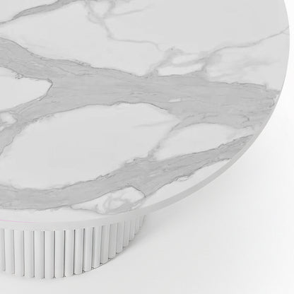 Close-up of a round dining table featuring a white stone top with grey marble veining and a white fluted pedestal base.