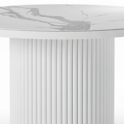 Close-up of a round dining table featuring a white stone top with grey marble veining and a matching white fluted pedestal base.