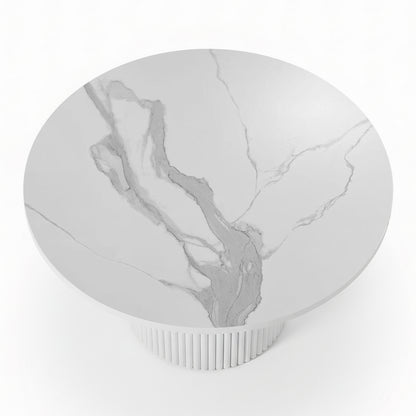 Close-up of a round dining table featuring a white stone top with grey marble veining and a white fluted pedestal base_2